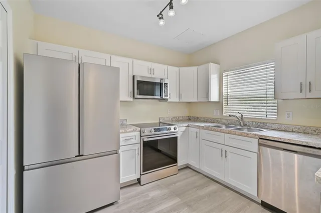 a kitchen with stainless steel appliances granite countertop white cabinets a sink a stove a refrigerator and white cabinets