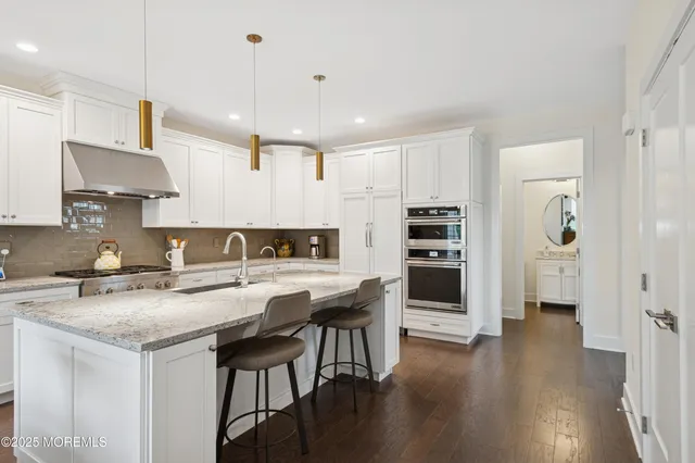 a kitchen with stainless steel appliances granite countertop a stove top oven a sink a refrigerator and white cabinets with wooden floor