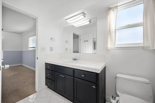 a bathroom with a toilet a sink a mirror a window and vanity