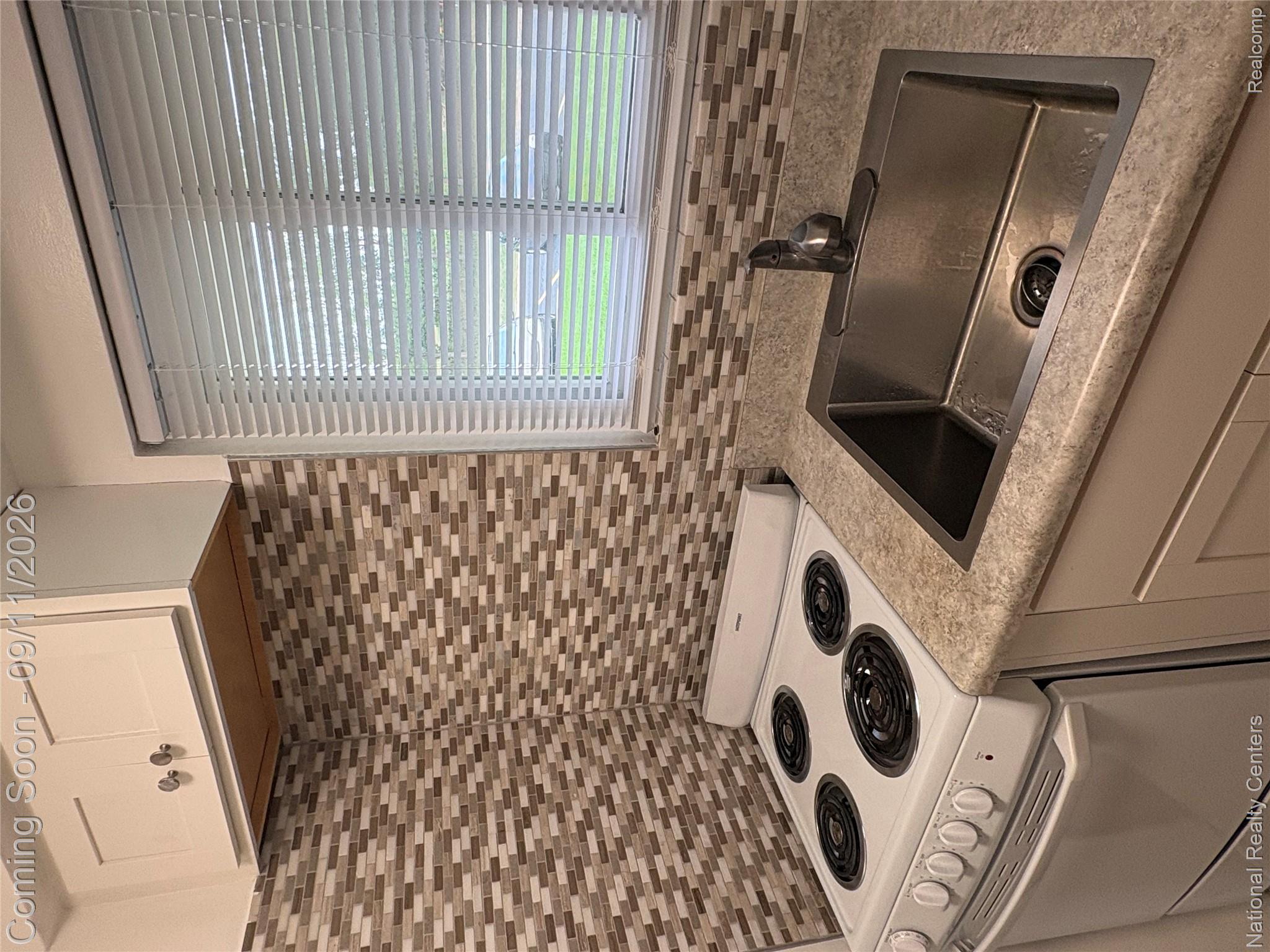 26945 Milford Road, Unit 3 New Hudson, MI 48165 - Photo 13 of 27 White upper cabinetry with knob hardware, mosaic tile backsplash, laminate countertop, stainless steel sink with faucet, and a range