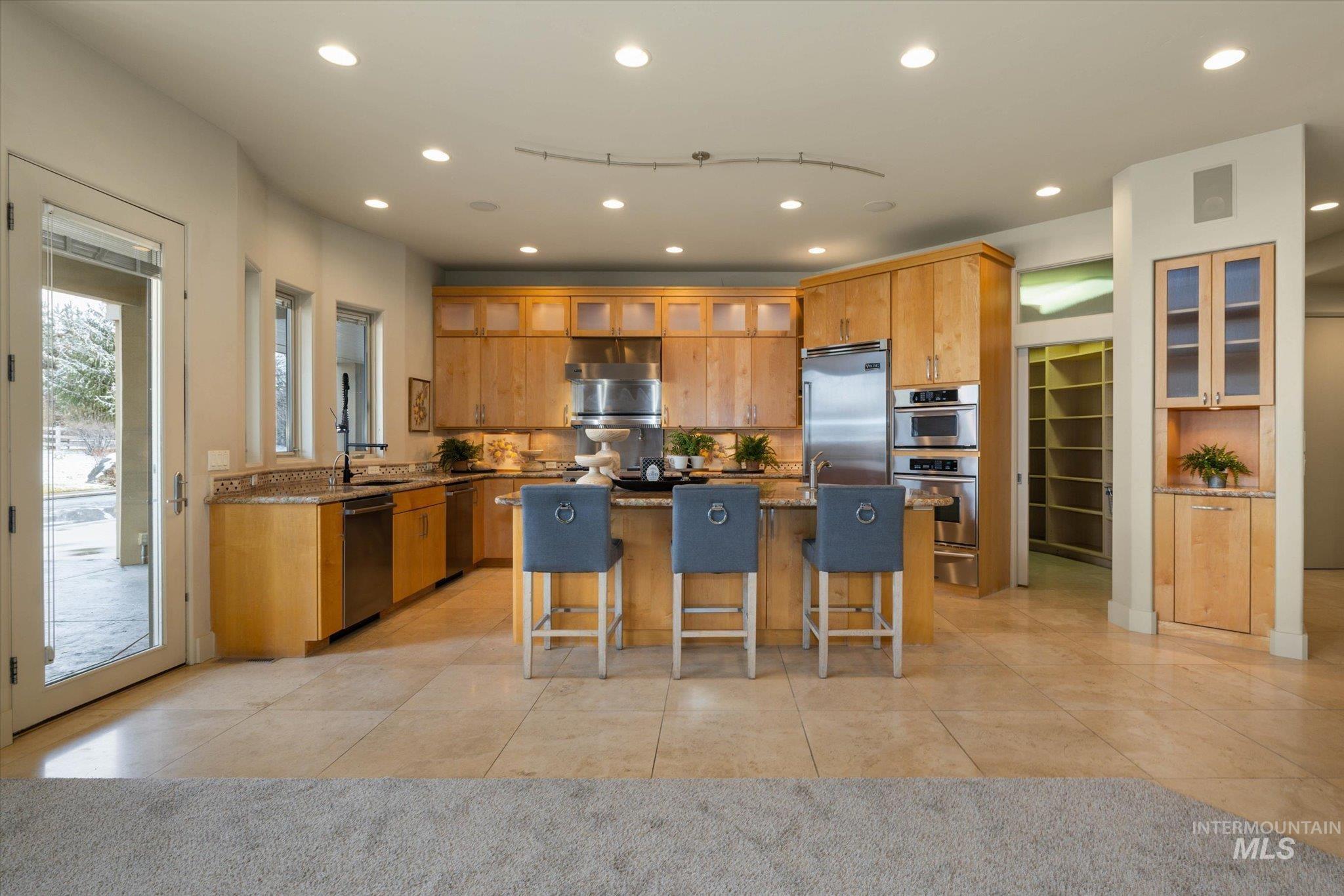 1400 North Razza Way Eagle, ID 83616 - Photo 14 of 50 Kitchen featuring glass fronted cabinets, a kitchen bar, recessed lighting, a center island with sink, and light stone counters