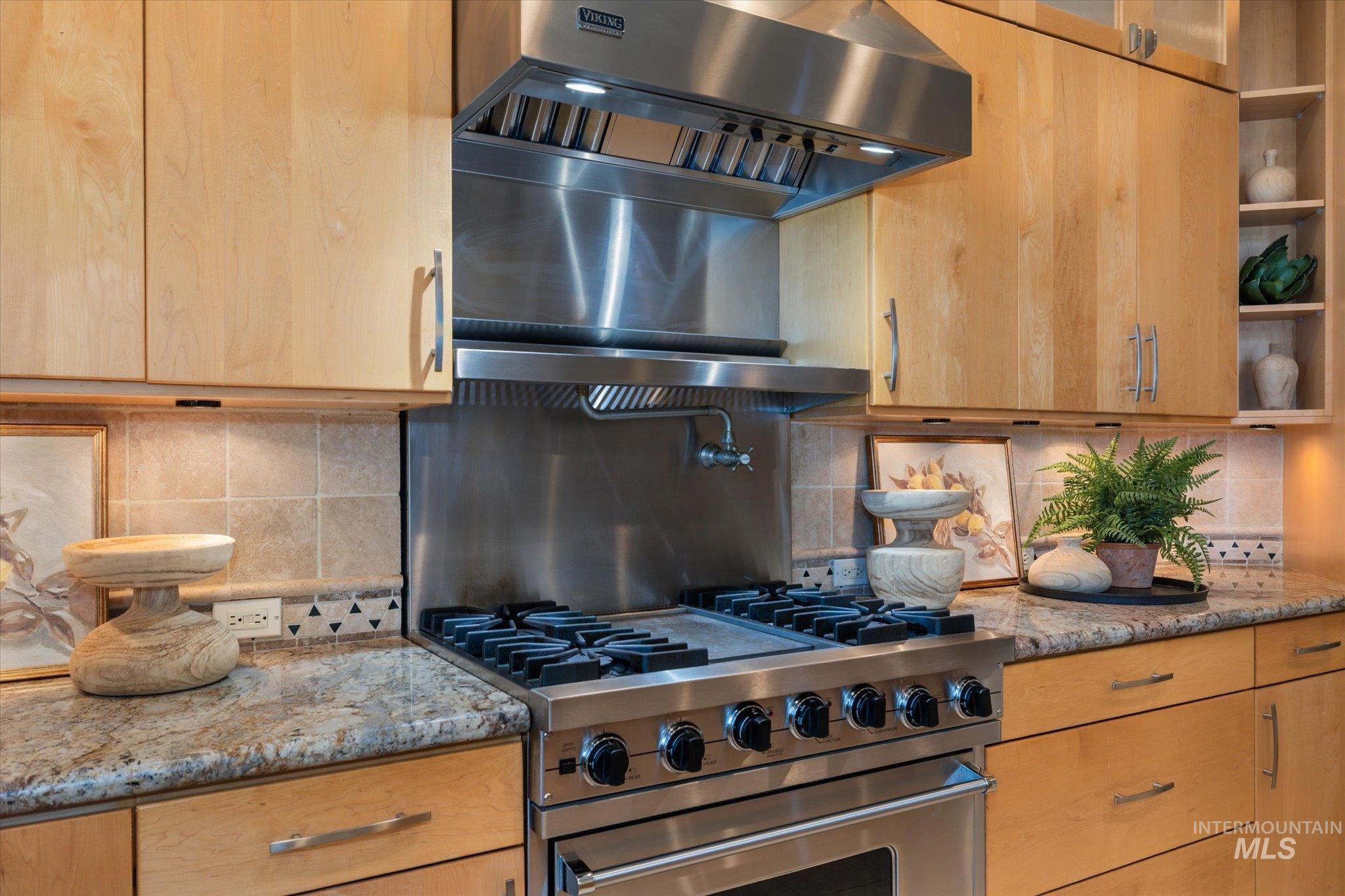 1400 North Razza Way Eagle, ID 83616 - Photo 16 of 50 Kitchen featuring backsplash, range hood, stainless steel range, light stone countertops, and glass insert cabinets