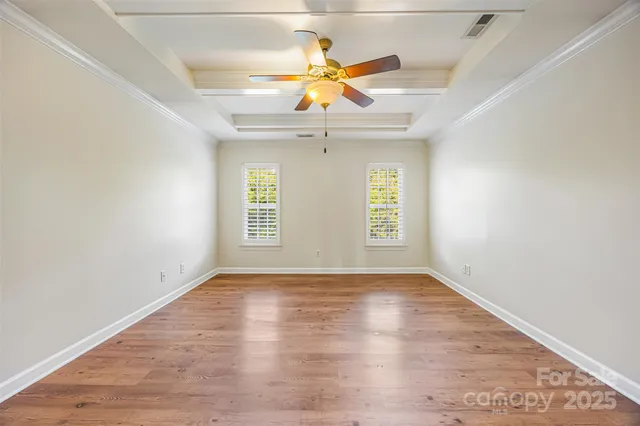 an empty room with wooden floor chandelier fan and windows