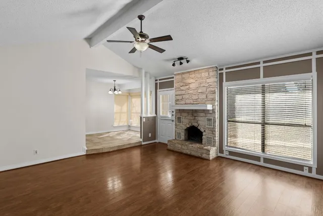 a view of an empty room with wooden floor fireplace and a window