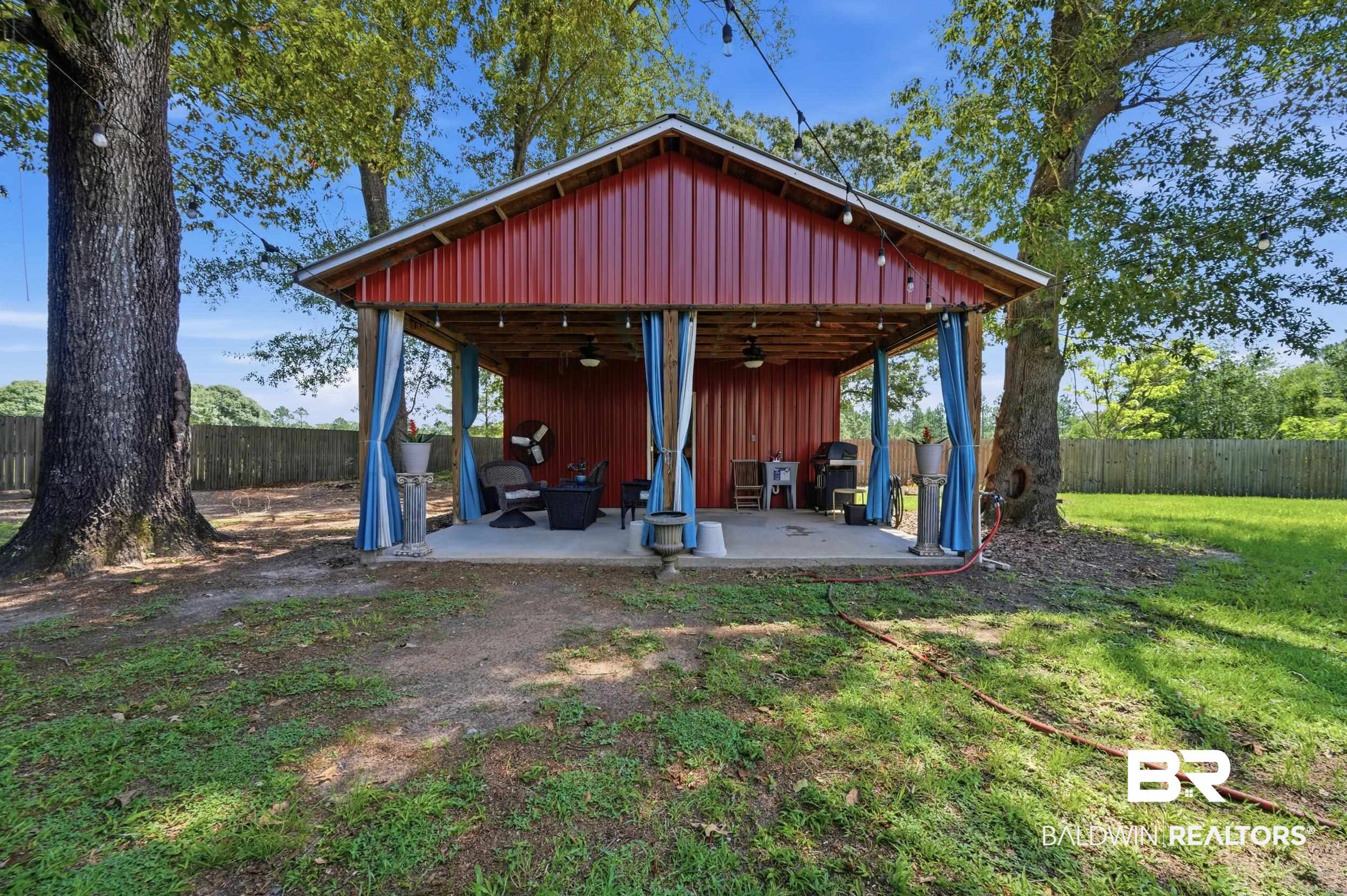 51620 Robert White Road Bay Minette, AL 36507 - Photo 66 of 81 Red metal-sided open-air structure featuring a concrete slab foundation, exposed wood beam ceiling, and string lighting