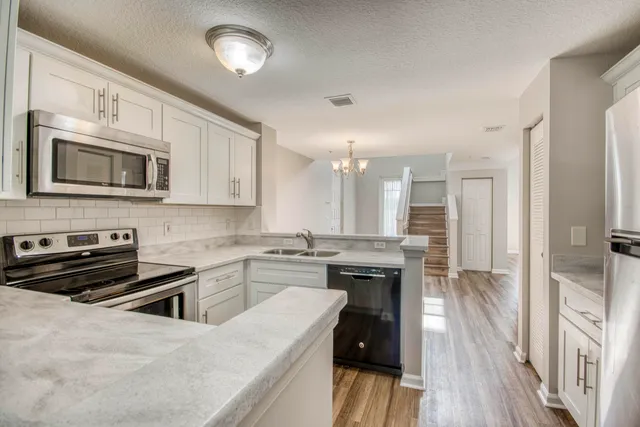 a kitchen with sink a refrigerator and white cabinets with wooden floor