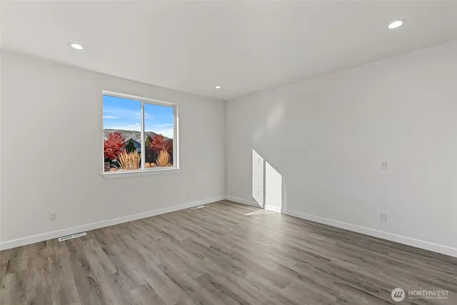 a view of an empty room with wooden floor and window
