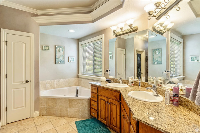 316 Azure Circle Draper, UT 84020 - Photo 22 of 48 Double vanity with granite countertop and integrated sinks, corner soaking tub with tiled surround, wood cabinetry, and crown molding details