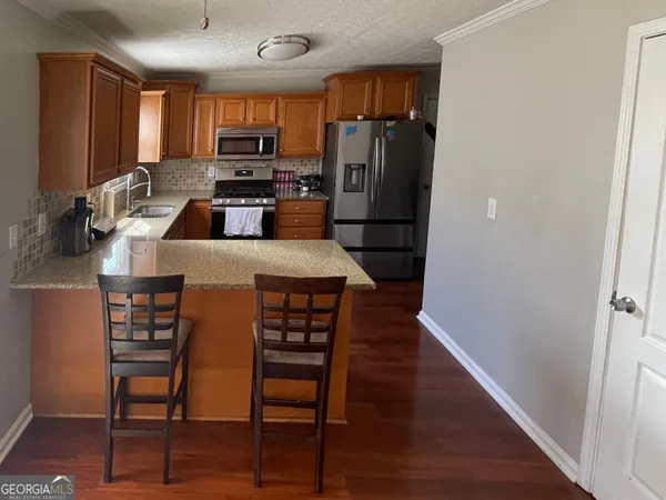 a kitchen with stainless steel appliances a refrigerator a stove a sink a dining table and chairs with wooden floor
