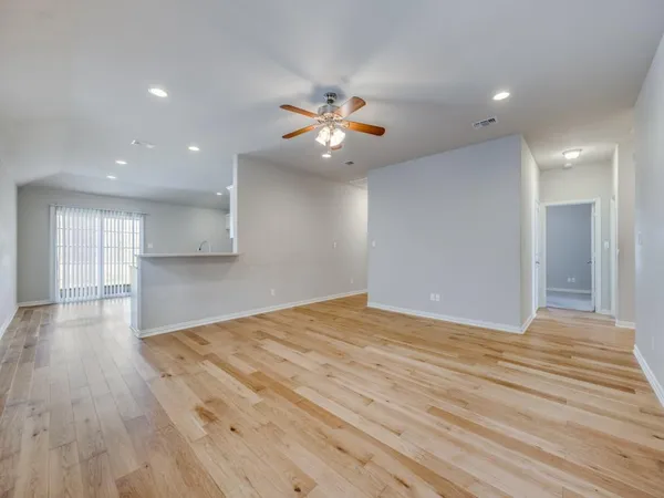 a view of an empty room and kitchen view with wooden floor