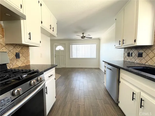 a kitchen with granite countertop a stove a sink dishwasher and white cabinets with wooden floor