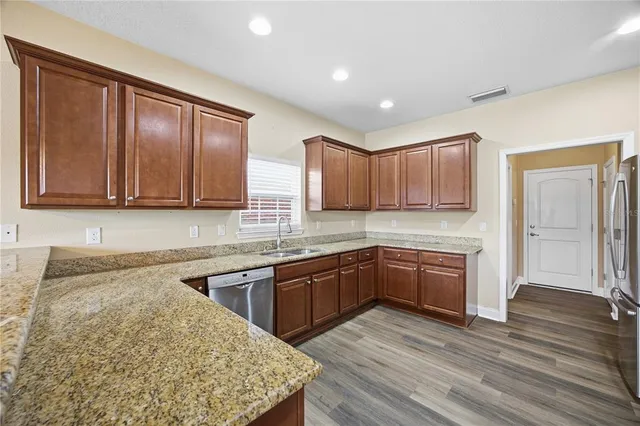 a kitchen with stainless steel appliances granite countertop wooden cabinets a sink and dishwasher a refrigerator with wooden floor