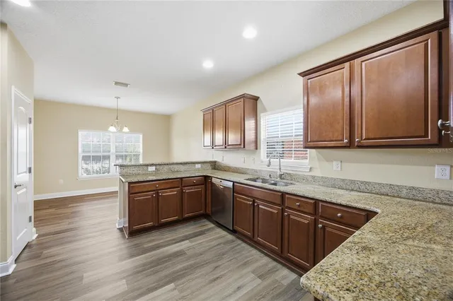 a kitchen with stainless steel appliances granite countertop wooden cabinets a sink dishwasher a stove and a refrigerator with wooden floor