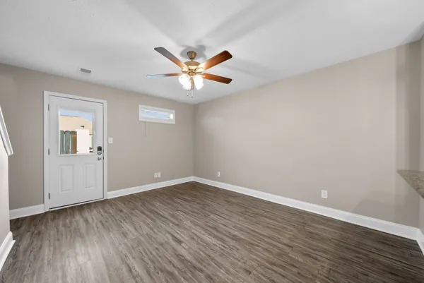 a view of an empty room with wooden floor and a ceiling fan