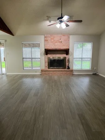 an empty room with wooden floor fireplace cabinet and windows