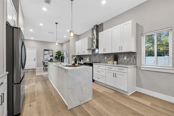 a large kitchen with stainless steel appliances granite countertop a stove a sink a refrigerator and white cabinets with wooden floor