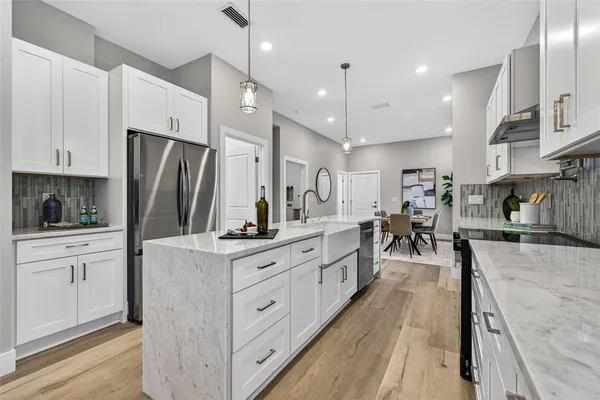 a kitchen with stainless steel appliances kitchen island granite countertop a refrigerator a stove a sink and white cabinets with wooden floor