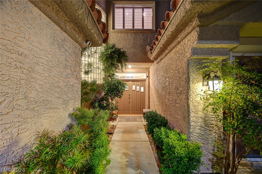 7995 Rio Rico Drive Las Vegas, NV 89113 - Photo 53 of 92 An inviting entryway leads to a double-door entrance, framed by lush greenery and warm sconce lighting.