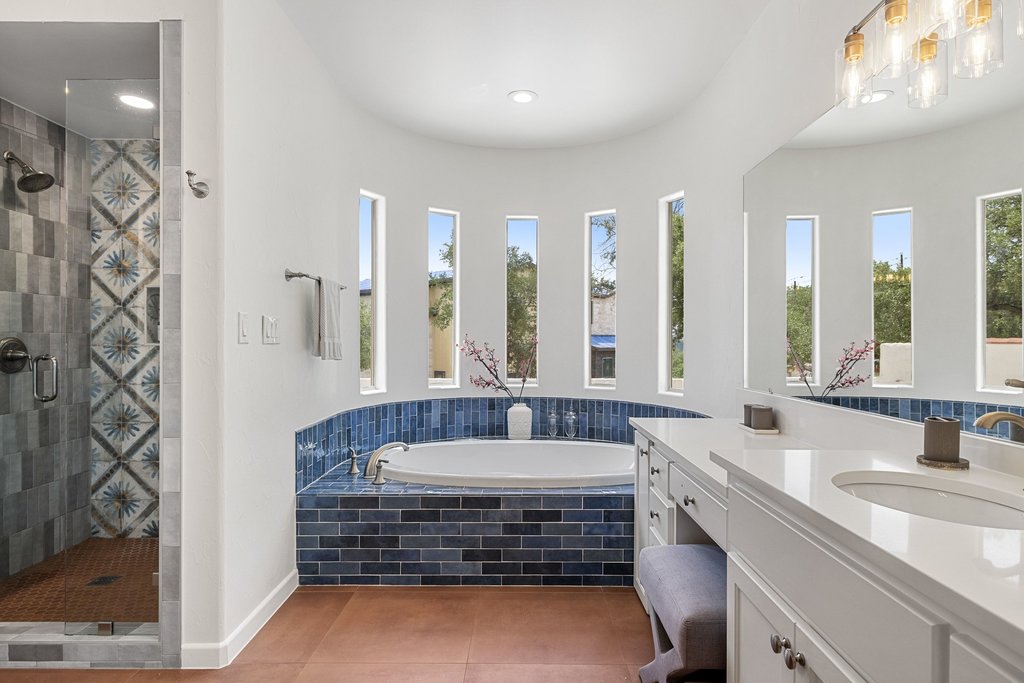 716 North Commons Ford Road Austin, TX 78733 - Photo 12 of 30 Bathroom featuring a built-in soaking tub with blue tile surround, multiple vertical windows, a glass-enclosed shower with decorative tile accents, a dual vanity with white countertops, and warm-toned flooring