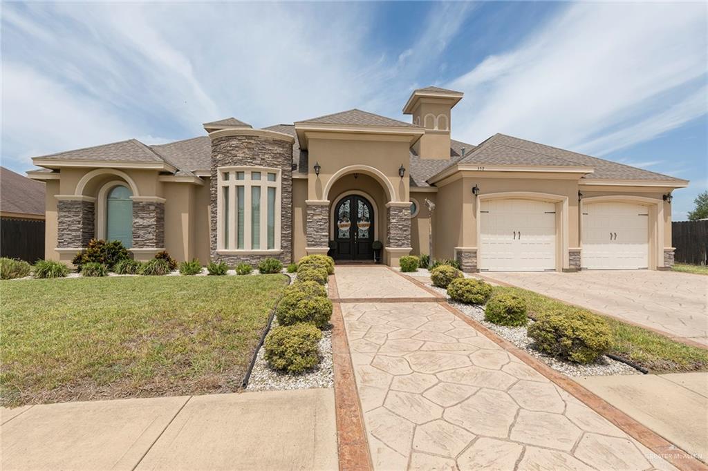 Mediterranean / spanish house with stone siding, french doors, stucco siding, a garage, and a front yard