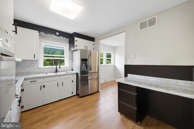 a kitchen with stainless steel appliances kitchen island granite countertop a refrigerator a sink dishwasher a oven with white cabinets and wooden floor
