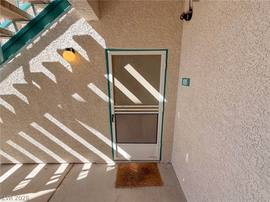 5211 South Lindell Road, Unit 105 Las Vegas, NV 89118 - Photo 16 of 19 A private entrance features stucco walls and a storm door beneath a staircase.
