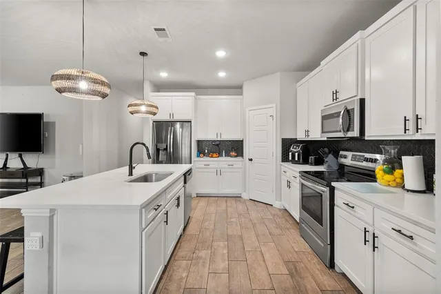 a large white kitchen with stainless steel appliances granite countertop a stove a sink a refrigerator and a wooden floor