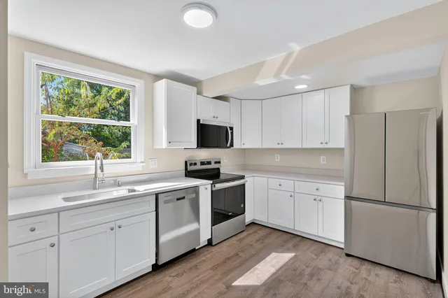 a kitchen with white cabinets appliances a sink and a window