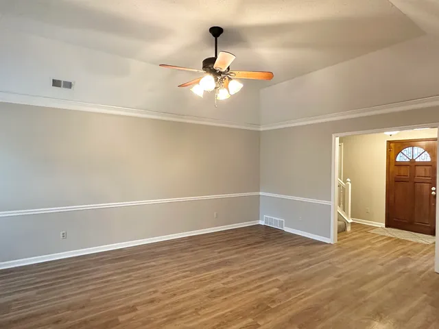 an empty room with wooden floor fan and windows