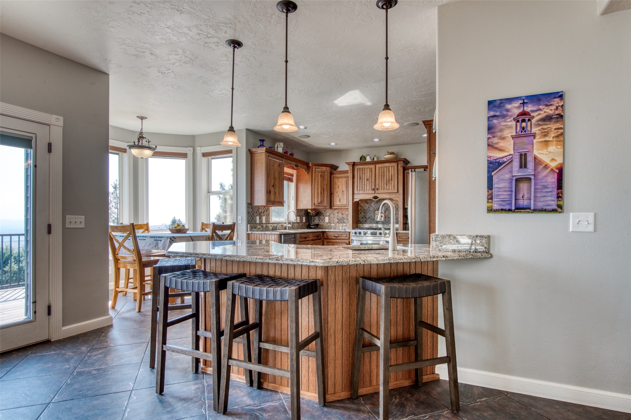 16374 Folsom Road Florence, MT 59833 - Photo 33 of 98 Kitchen featuring brown cabinets, a kitchen breakfast bar, light stone countertops, pendant lighting, and a textured ceiling