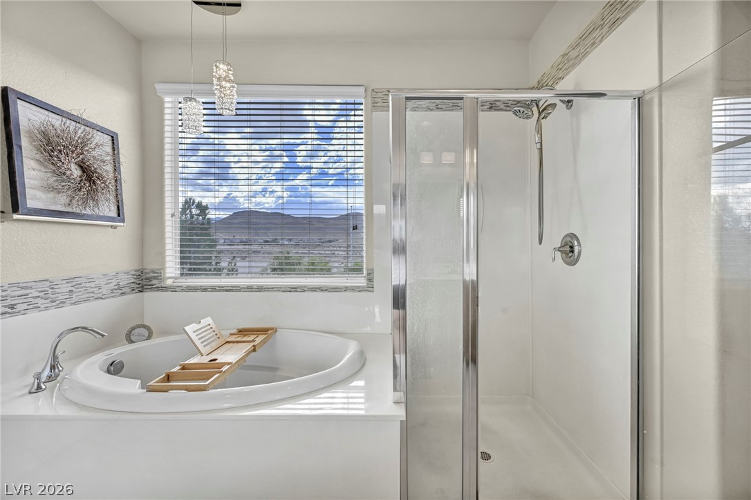 389 Fringe Ruff Drive Las Vegas, NV 89148 - Photo 22 of 53 A glass-enclosed walk-in shower stands adjacent to a deep soaking tub beneath scenic window views.