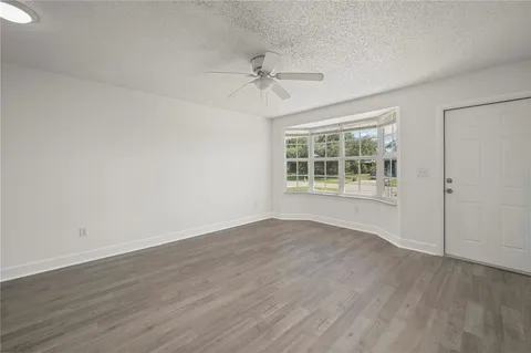 an empty room with wooden floor chandelier fan and windows