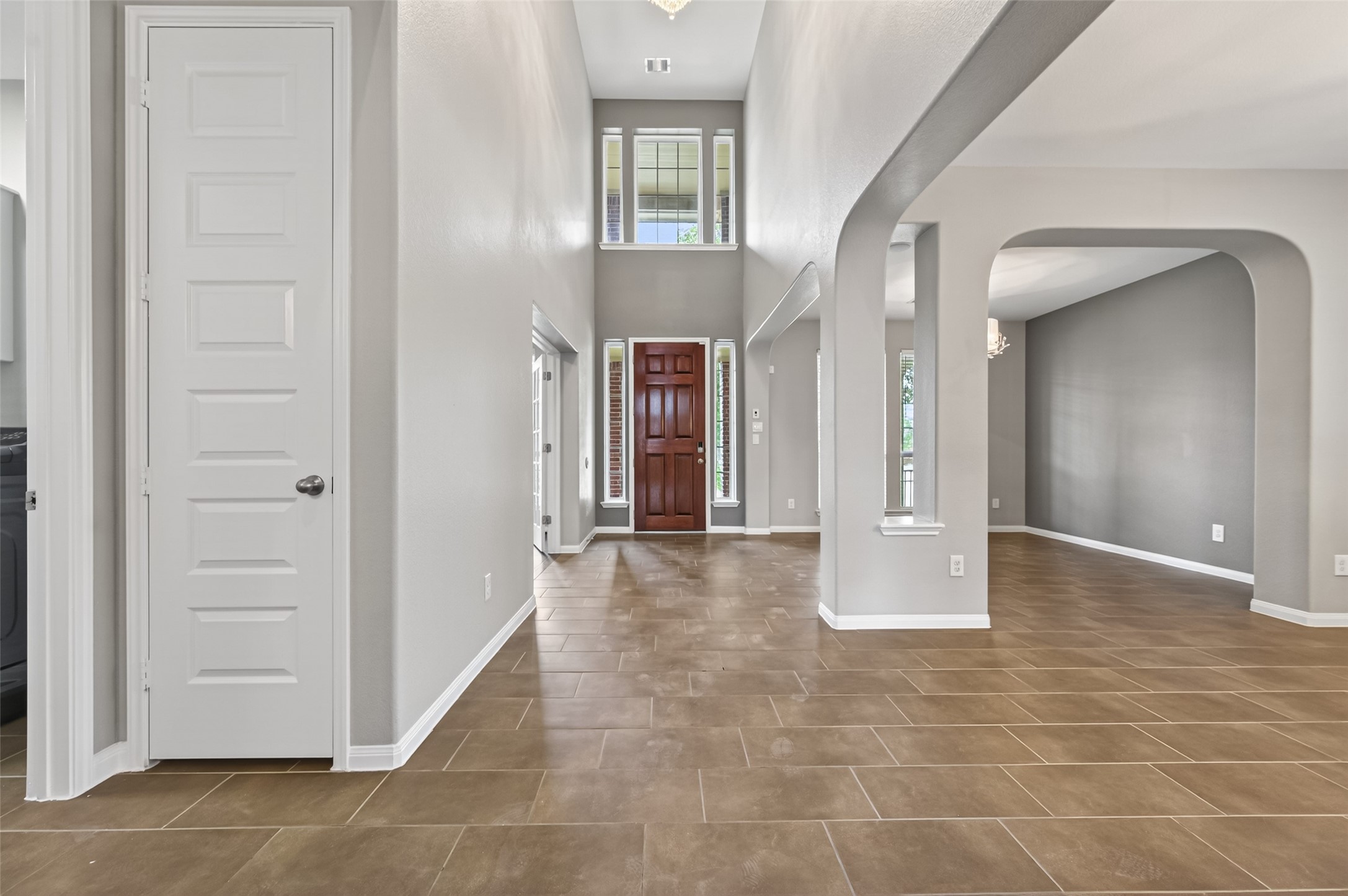 7003 Bristol Memorial Drive Spring, TX 77379 - Photo 11 of 40 Welcoming entry in this Spring TX 77379 home featuring soaring ceilings, large transom windows, and durable tile flooring that extends throughout the main level. The wood front door with sidelights provides natural light and a strong first impression. Arched openings lead into a flexible formal living or dining space, offering versatility for entertaining or everyday use. Neutral interior tones and open sightlines enhance the spacious feel in this move-in ready home