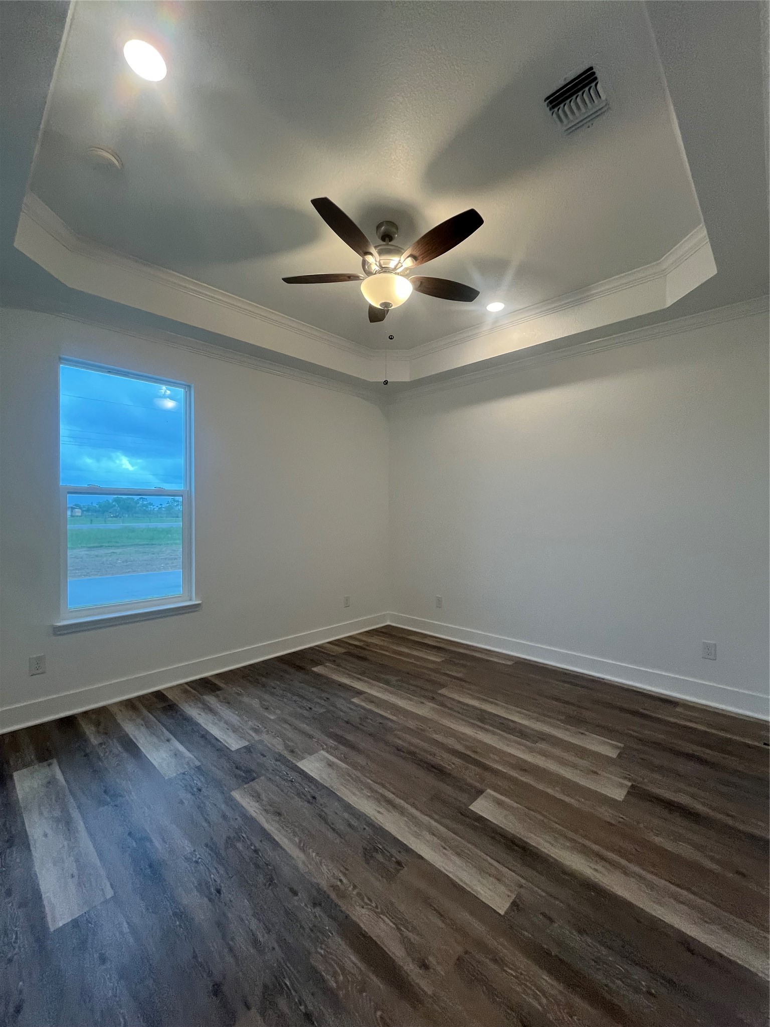 33416 FM 521 Road Angleton, TX 77515 - Photo 19 of 20 This room features a modern design with a tray ceiling, recessed lighting, and a ceiling fan. It has a large window for natural light and medium gray/wood water proof plank flooring, creating a warm and inviting atmosphere.