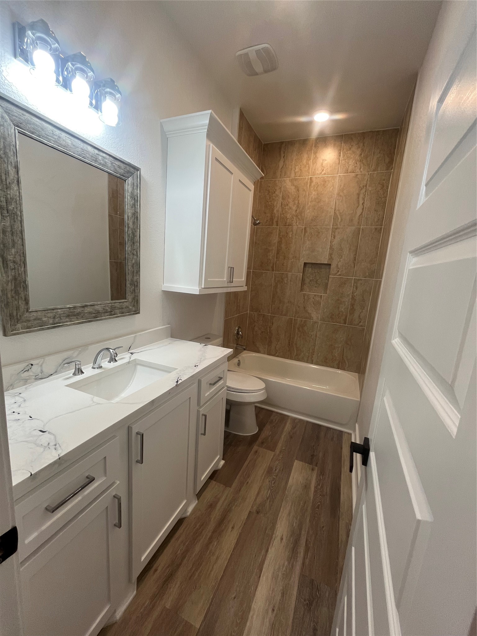 33416 FM 521 Road Angleton, TX 77515 - Photo 20 of 20 This bathroom features a sleek design with medium gray/ wood water proof flooring, a white vanity with a Quartz countertop, and ample storage. The shower-tub combo is accented with warm, textured tiles, and bright lighting enhances the space.