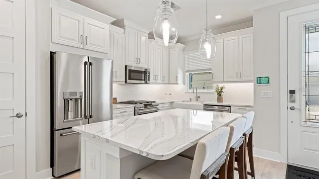 a kitchen with stainless steel appliances granite countertop a stove a refrigerator a sink a stove and white cabinets with wooden floor