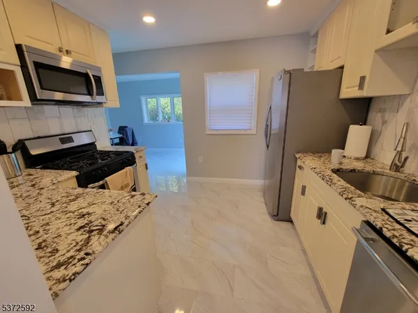 a kitchen with granite countertop a sink a stove top oven a refrigerator a counter space and cabinets
