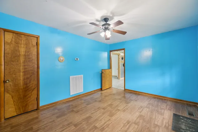 an empty room with wooden floor chandelier fan and windows