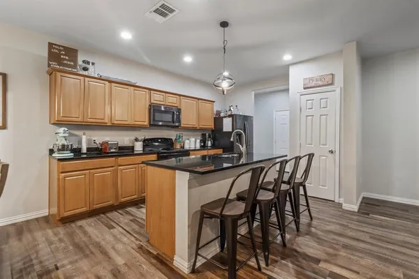a kitchen with stainless steel appliances granite countertop a stove top oven a sink a refrigerator with a dining table and chairs with wooden floor