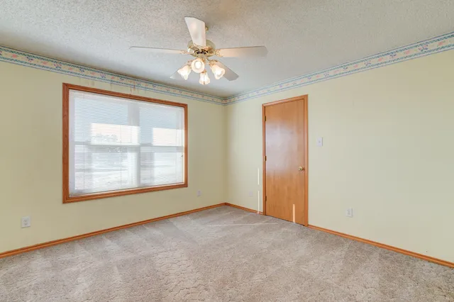 an empty room with a chandelier fan and windows