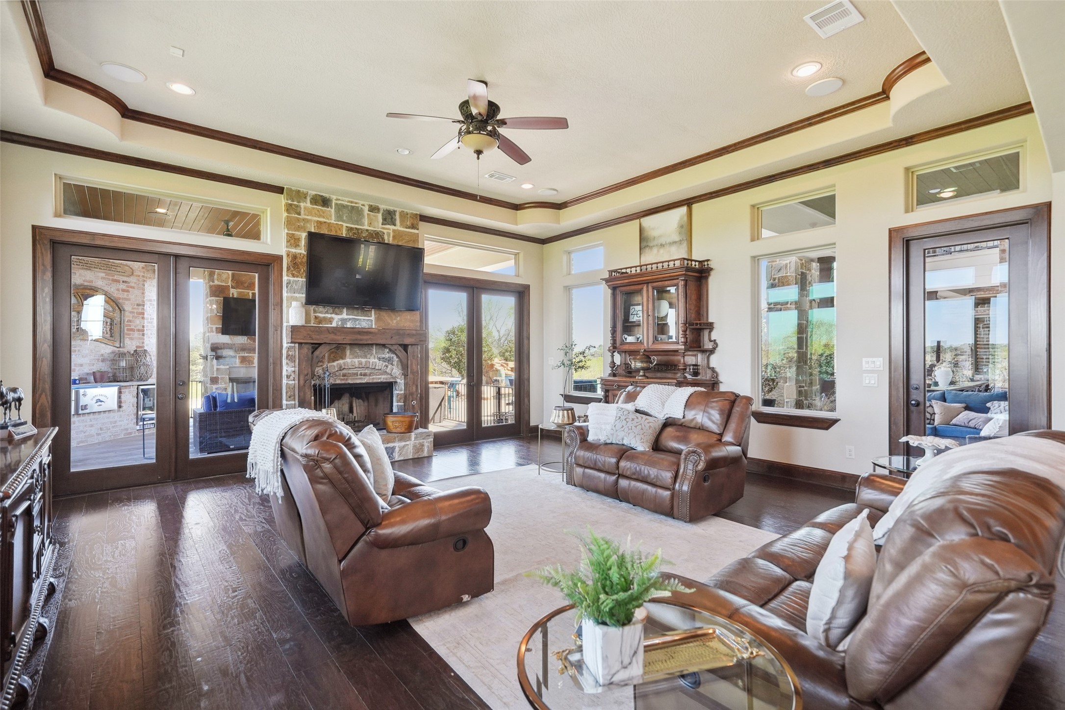 460 Bishop Road Huntsville, TX 77320 - Photo 11 of 50 The living room features a stunning stone fireplace with a cedar mantle, complemented by beautifully crafted wood trim. The space seamlessly connects to the kitchen, creating an open and inviting atmosphere. Two sets of double French doors lead to an outdoor entertainment living area, allowing for effortless indoor-outdoor flow. Expansive windows frame breathtaking views, bringing in ample natural light and enhancing the warmth of the space.