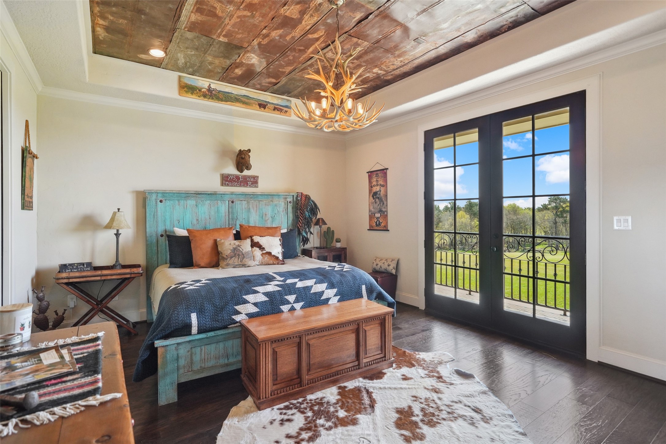 460 Bishop Road Huntsville, TX 77320 - Photo 20 of 50 Expansive bedroom with rich wood flooring, a walk-in closet, and elegant French doors opening to a balcony. The ceiling features a tray design with antique pressed tin, complemented by an antler chandelier.
