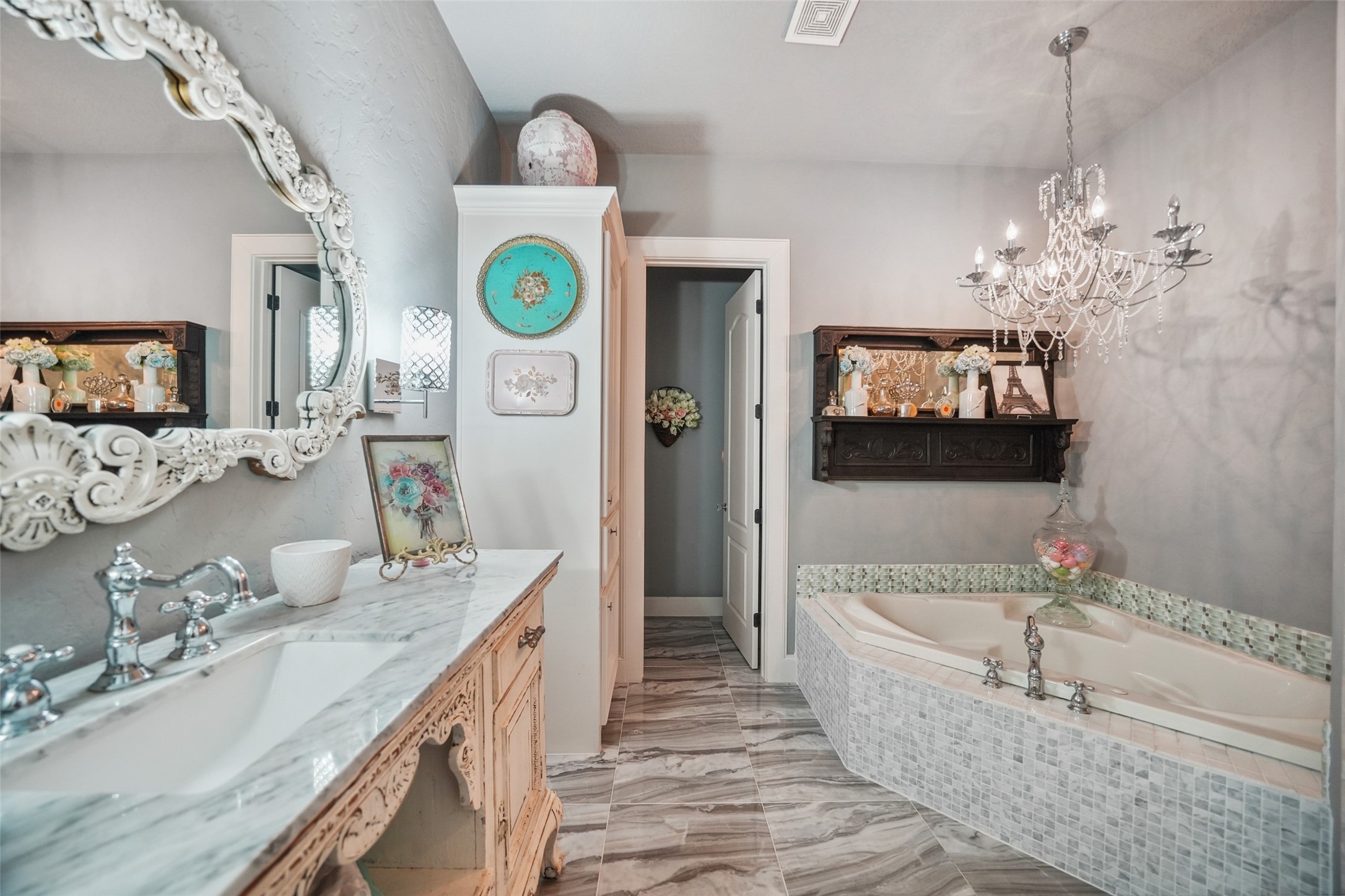 460 Bishop Road Huntsville, TX 77320 - Photo 25 of 50 The ensuite bathroom boasts a luxurious jacuzzi tub beneath a striking chandelier, a walk-in shower with elegant stone accents and travertine, and a granite vanity area with a travertine sink.