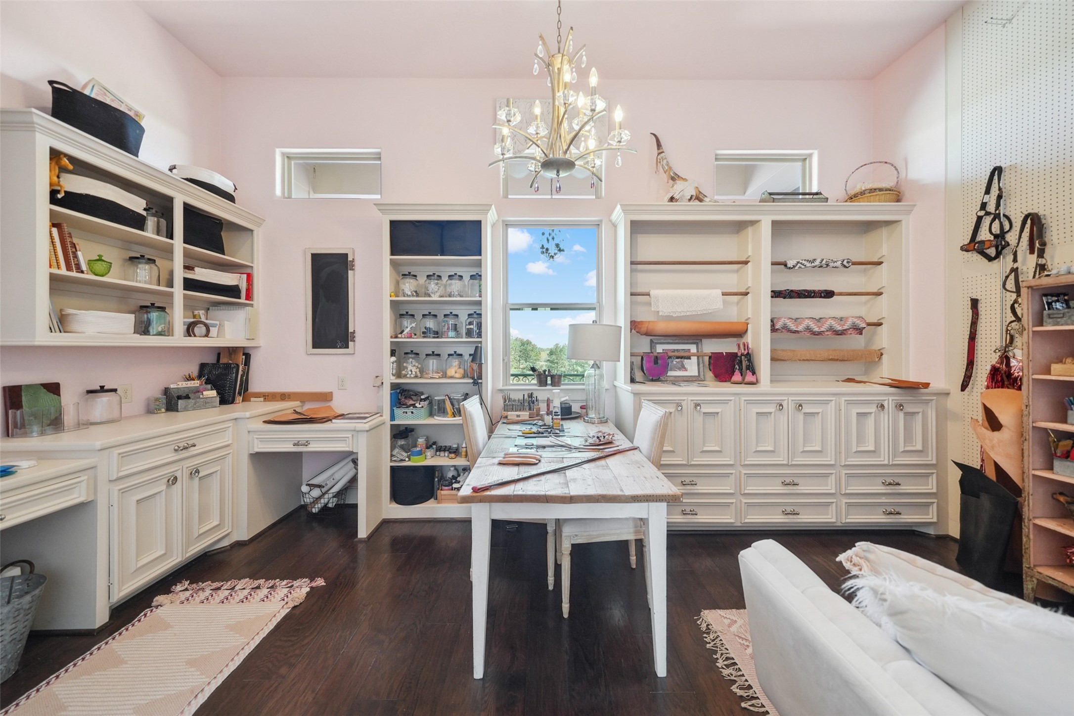 460 Bishop Road Huntsville, TX 77320 - Photo 26 of 50 This well-designed upstairs craft room features two built-in desk areas with knee space, offering ample workspace. Custom cabinetry and shelving provide abundant storage throughout the room. A central table serves as an additional workspace, ideal for creative projects. The room is enhanced by rich wood floors and a statement chandelier, creating a bright and inviting atmosphere.
