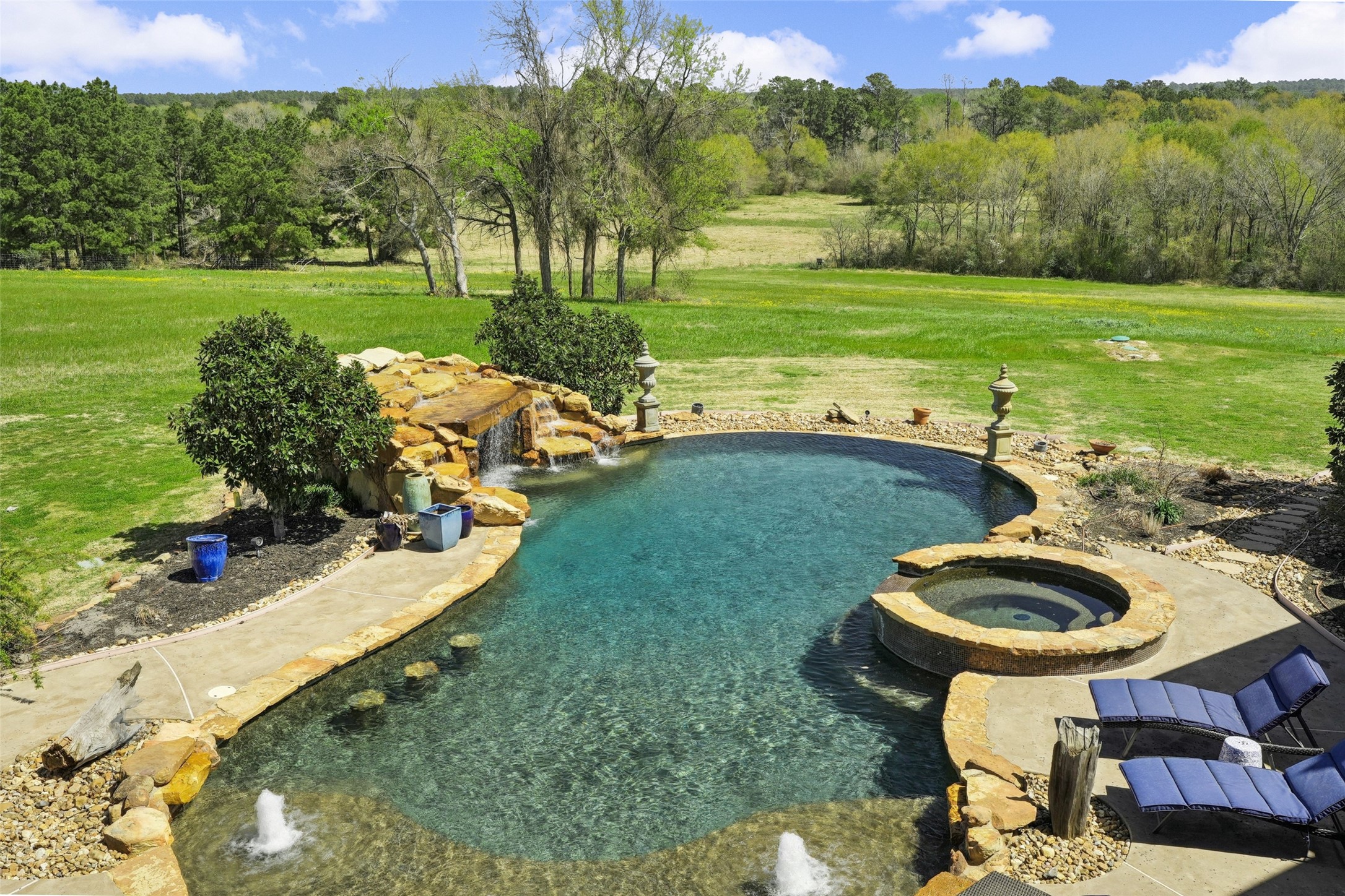 460 Bishop Road Huntsville, TX 77320 - Photo 32 of 50 An impressive 80,000-gallon saltwater pool with pebble tech features a stunning stone waterfall with a hidden grotto beneath. Built-in bar stools within the pool and bench seating inside the grotto create a luxurious and relaxing atmosphere.