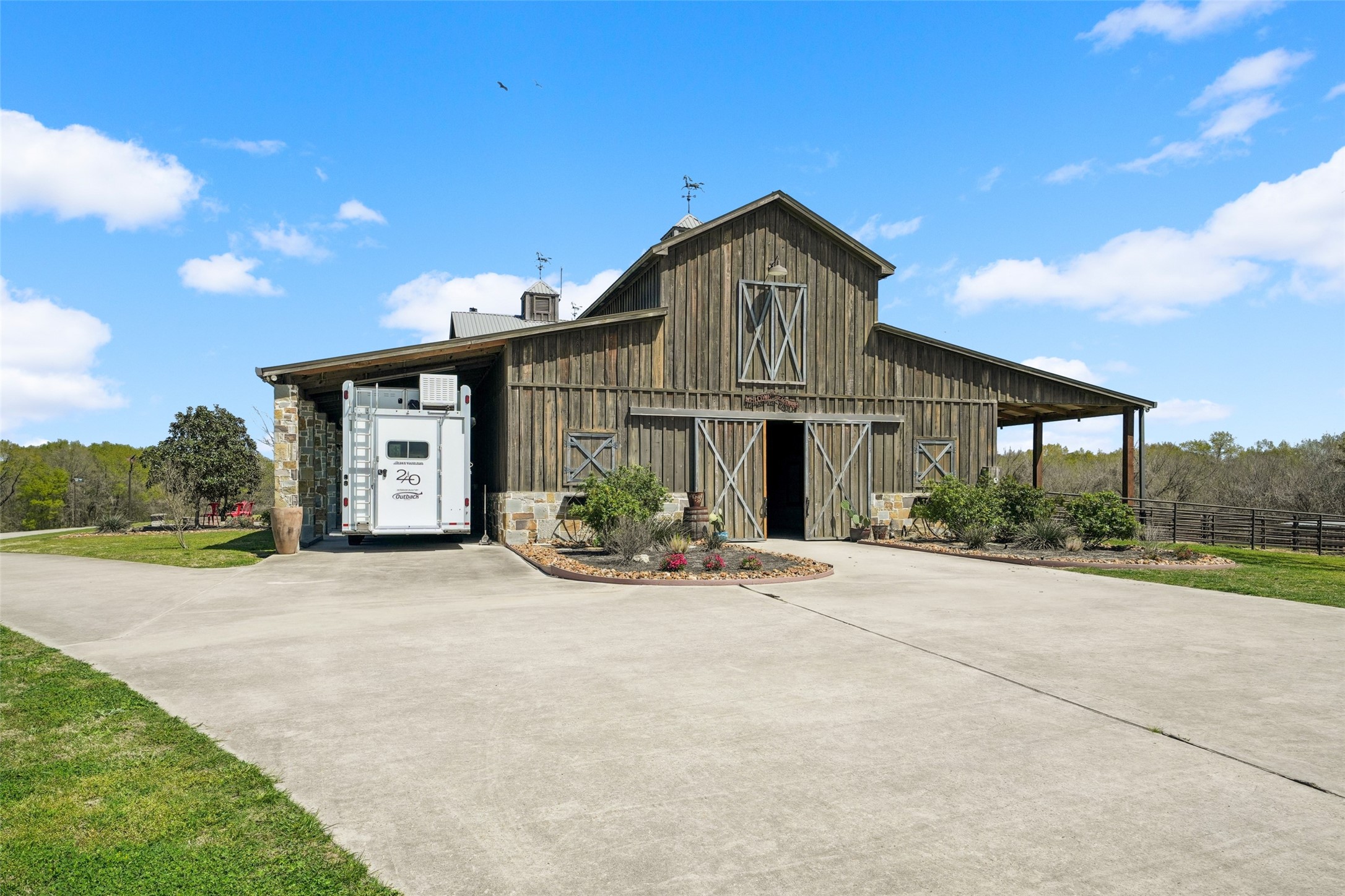 460 Bishop Road Huntsville, TX 77320 - Photo 42 of 50 Stunning custom barn blending rustic charm with modern convenience. Highlights include large sliding doors, covered trailer parking, and a beautifully landscaped entry. A concrete driveway ensures easy access, while spacious overhangs provide ample storage and workspace. Built with solid Arkansas stone and cypress siding, this impressive barn spans approximately 11,000 square feet—ideal for equestrian enthusiasts!