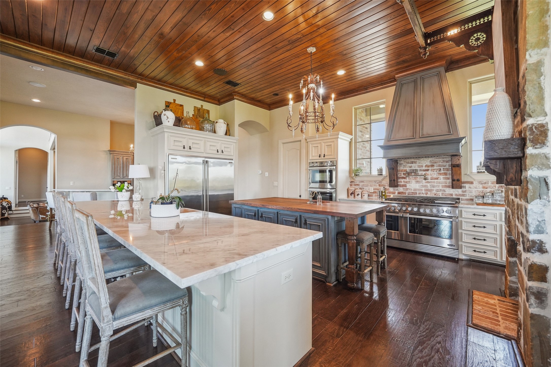 460 Bishop Road Huntsville, TX 77320 - Photo 9 of 50 This gourmet kitchen boasts a double-sided fireplace, Carrera marble countertops, and a spacious island with a butcher block top and copper sink. Features include a travertine farmhouse sink, a six-burner commercial gas range with dual ovens, two additional ovens, a warming drawer, and a full-size commercial fridge and freezer. A brick backsplash enhances its rustic charm.