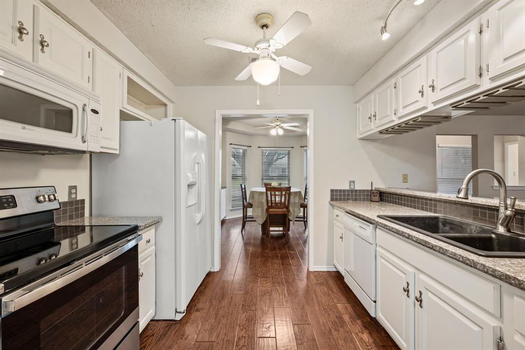 6605 Bluebonnet Drive Rowlett, TX 75089 - Photo 10 of 25 a kitchen with stainless steel appliances a sink dishwasher stove and white cabinets with wooden floor