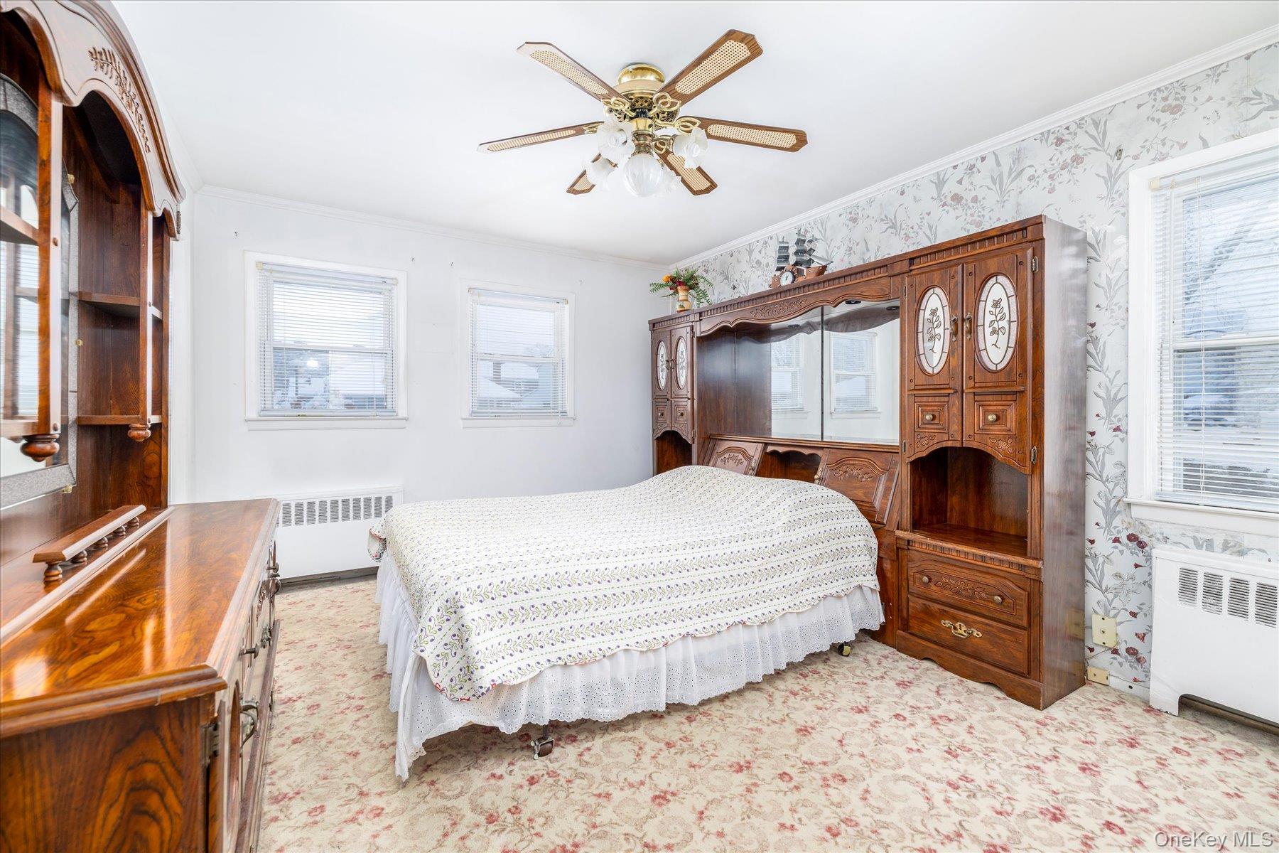 2934 Kinloch Road Wantagh, NY 11793 - Photo 15 of 30 Bedroom featuring radiator heating unit, ornamental molding, a ceiling fan, wallpapered walls, and light colored carpet