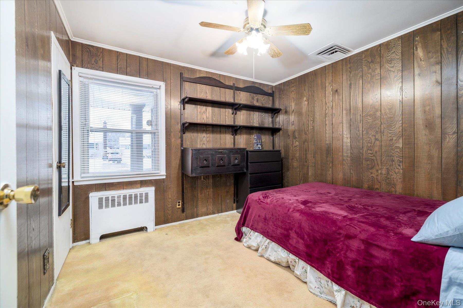 2934 Kinloch Road Wantagh, NY 11793 - Photo 19 of 30 Bedroom featuring wooden walls, radiator, light colored carpet, a ceiling fan, and crown molding